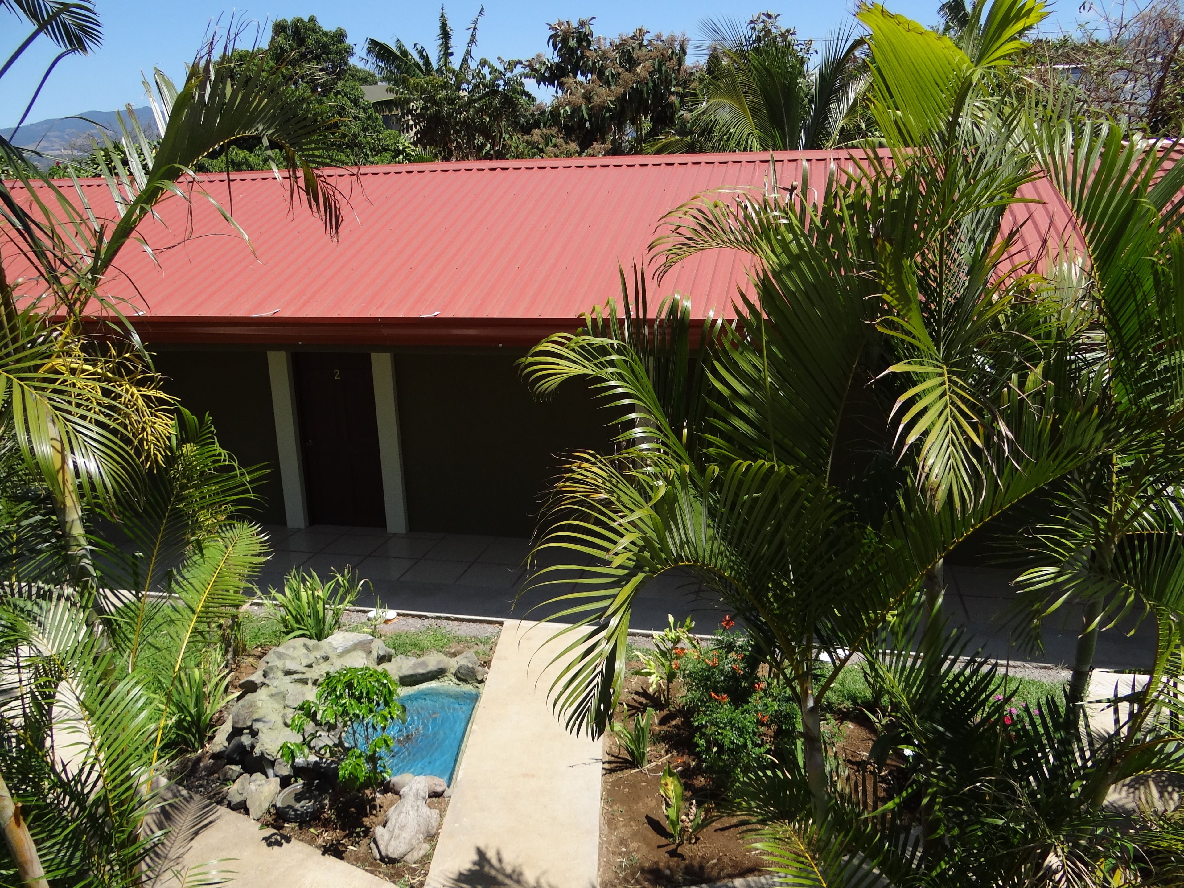 A building with a red roof, surrounded by lush greenery and a small pool area.