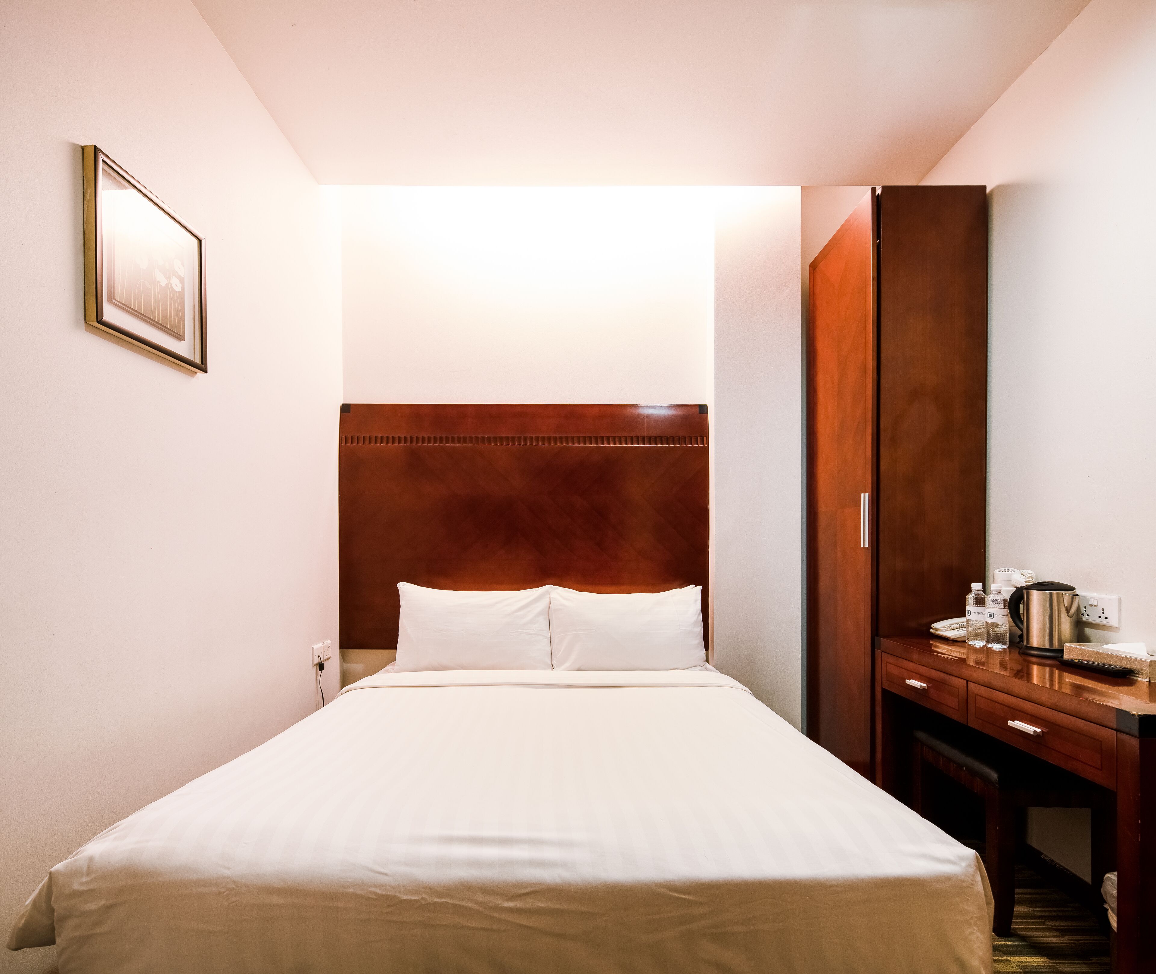 A hotel room with a large bed, a wooden headboard, a desk with a kettle, and a mirror.