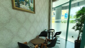 Un vestíbulo de hotel con una pared de mármol, un cuadro enmarcado, una pequeña mesa con sillas y una planta en maceta.