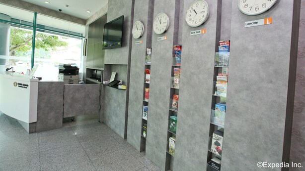 Un área de recepción con relojes que muestran diferentes husos horarios, un mostrador con una computadora y una pared con mapas.