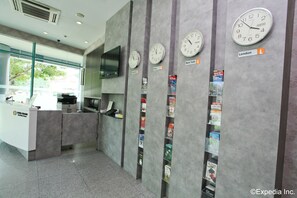 Un espace d’accueil avec des horloges indiquant différents fuseaux horaires, un comptoir avec un ordinateur et un mur où sont affichées des cartes.
