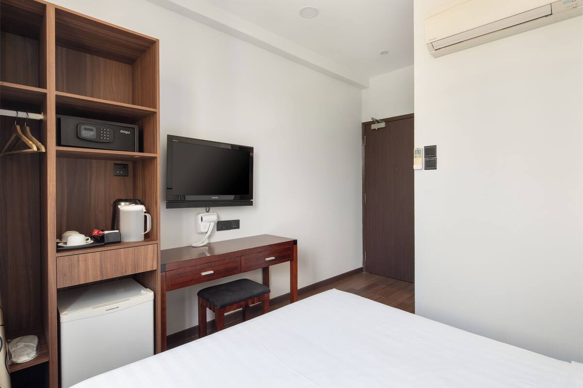 Habitación de hotel con un escritorio de madera, televisión, refrigerador pequeño, cama y armario.