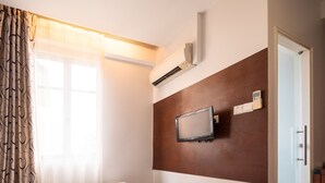 Una habitación de hotel con dos camas individuales, un televisor de pantalla plana montado en la pared, un equipo de aire acondicionado y una puerta que da a otra habitación.