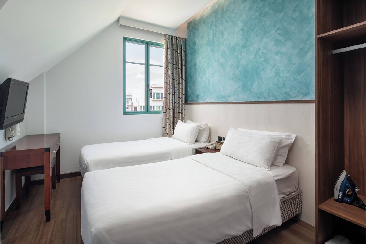 Habitación de hotel con dos camas, un escritorio, un televisor y una ventana con cortinas.
