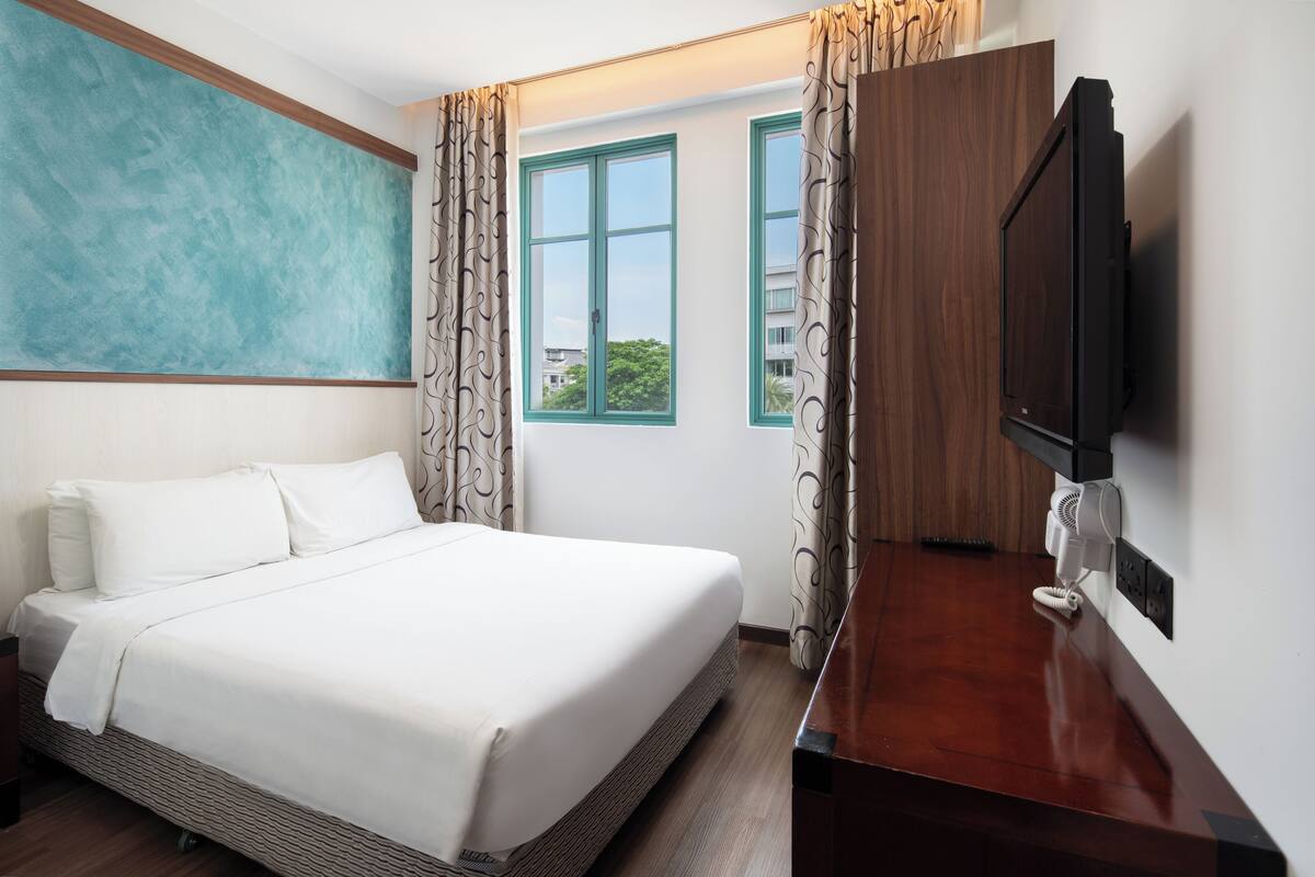 Una habitación de hotel con cama, televisión, escritorio y ventana con cortinas.