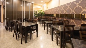 Un comedor amplio con varias mesas y sillas, un adorno de pared y una planta grande en maceta.