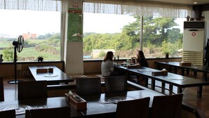 Un restaurante con mesas y sillas, amplias ventanas con vistas a zonas verdes y un ventilador de techo.
