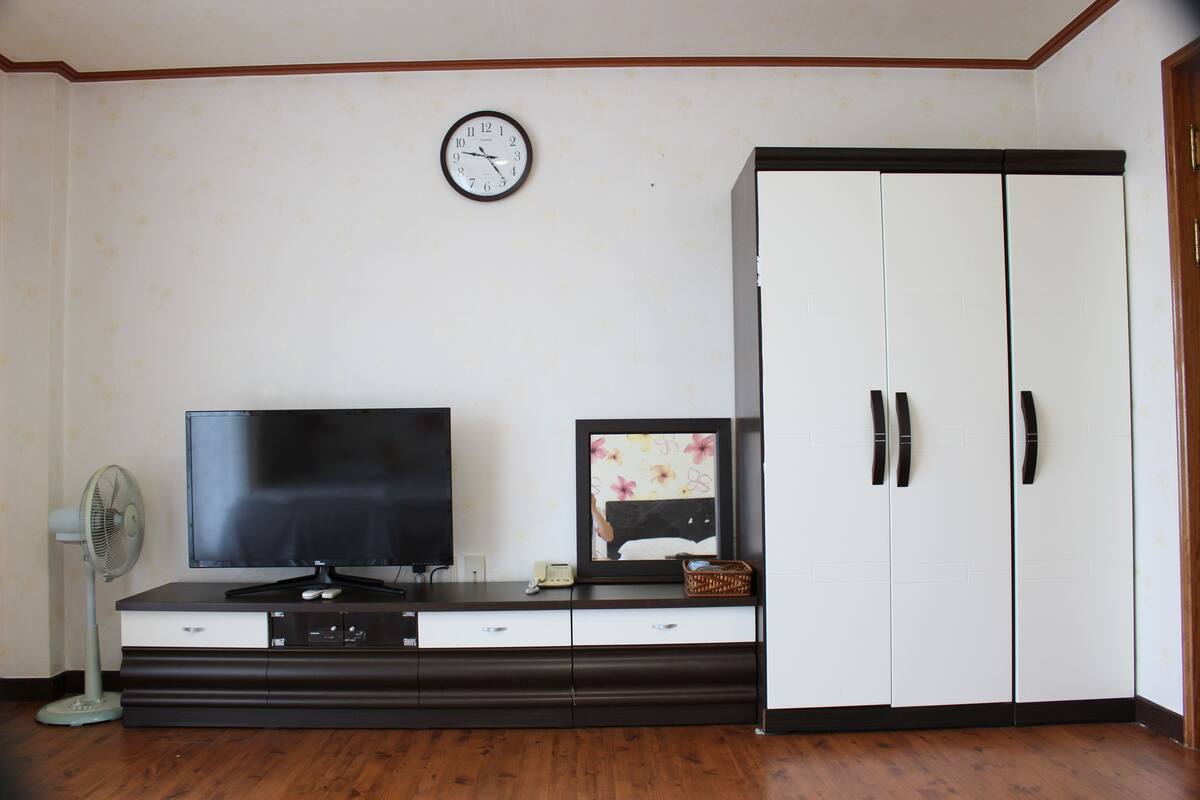 A room with a television, a clock, a cabinet, and a fan.