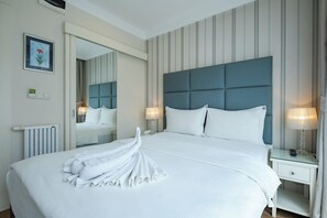 A neatly made bed with white linens and a towel arranged on the bed. There is a nightstand with a lamp and a telephone. The room has a striped wallpaper and a large mirror on the wall. - Ten Rooms Hotel Istanbul  (Istanbul)
