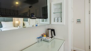 Ein Hotelzimmer mit Bett, Nachttisch mit Wasserkocher, Spiegel und Ablagefläche für Gläser.
