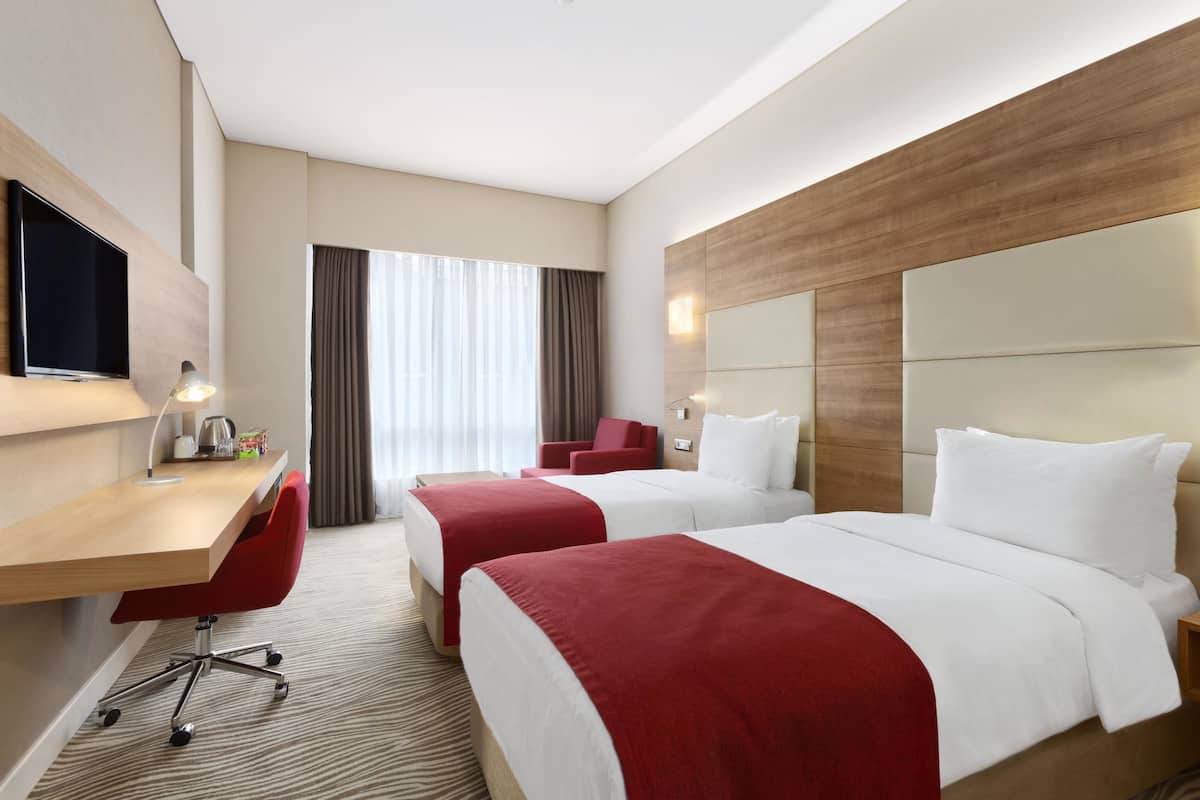 A hotel room with two beds, a desk with a chair, a TV, and a window with curtains.