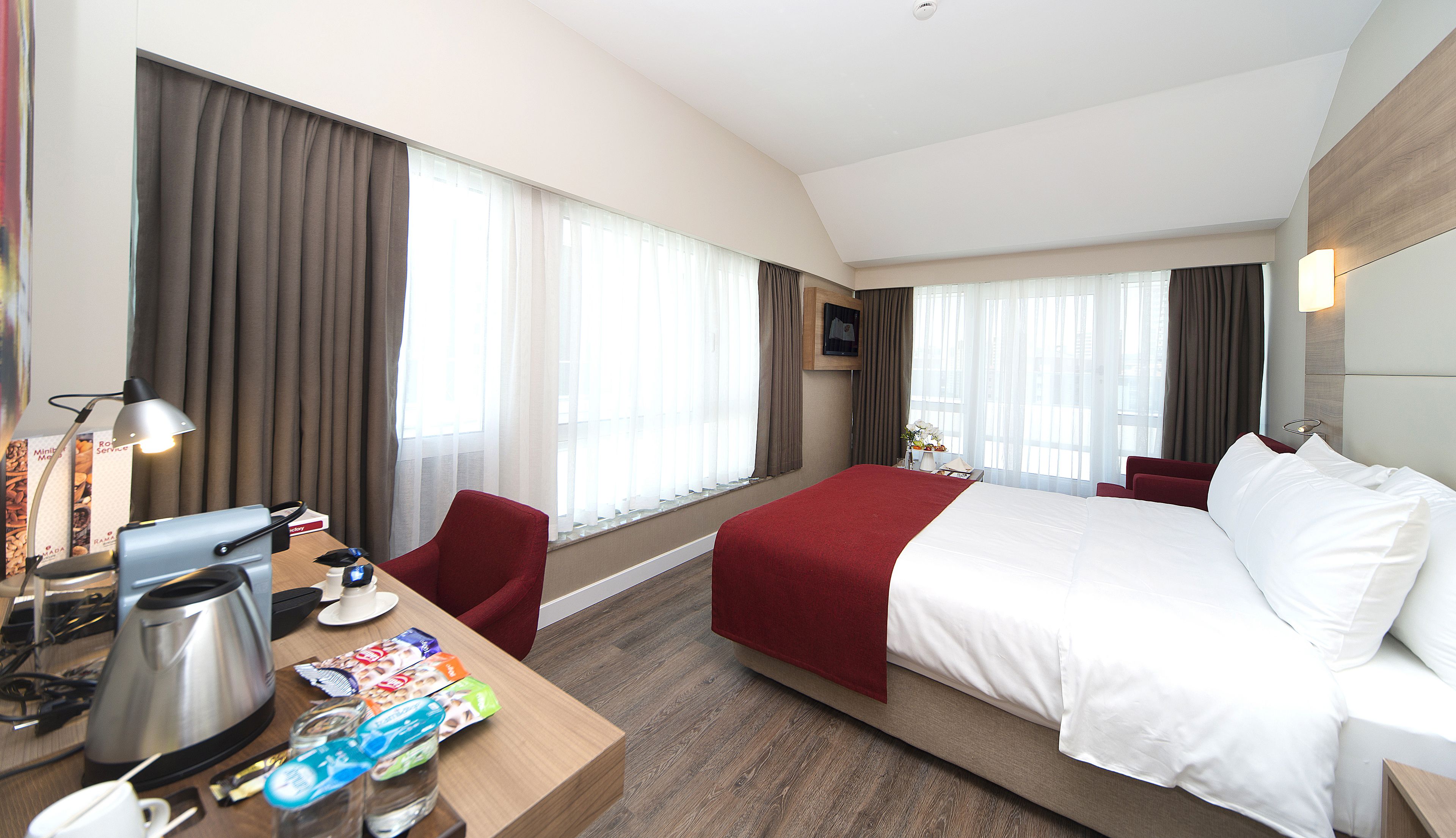 A hotel room with a large bed, a desk with a coffee maker, a chair, and a TV on the wall.