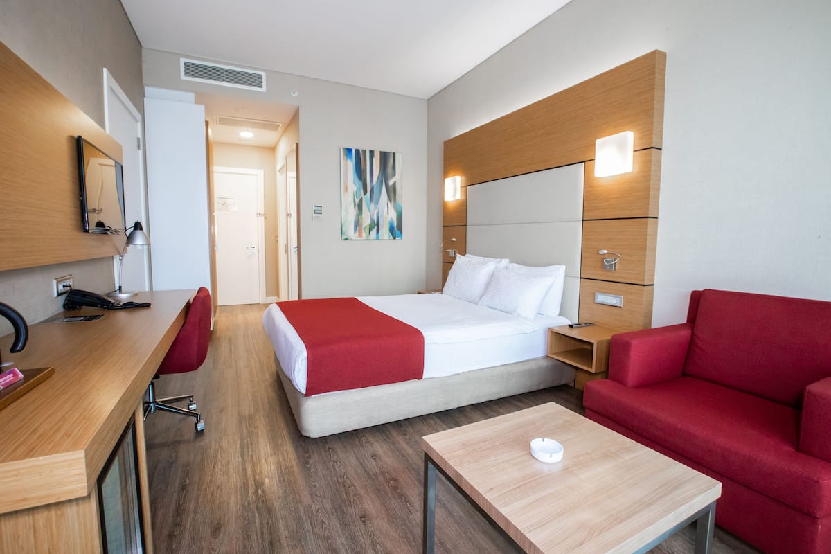 A modern hotel room with a bed, a desk, a red sofa, and a small table.
