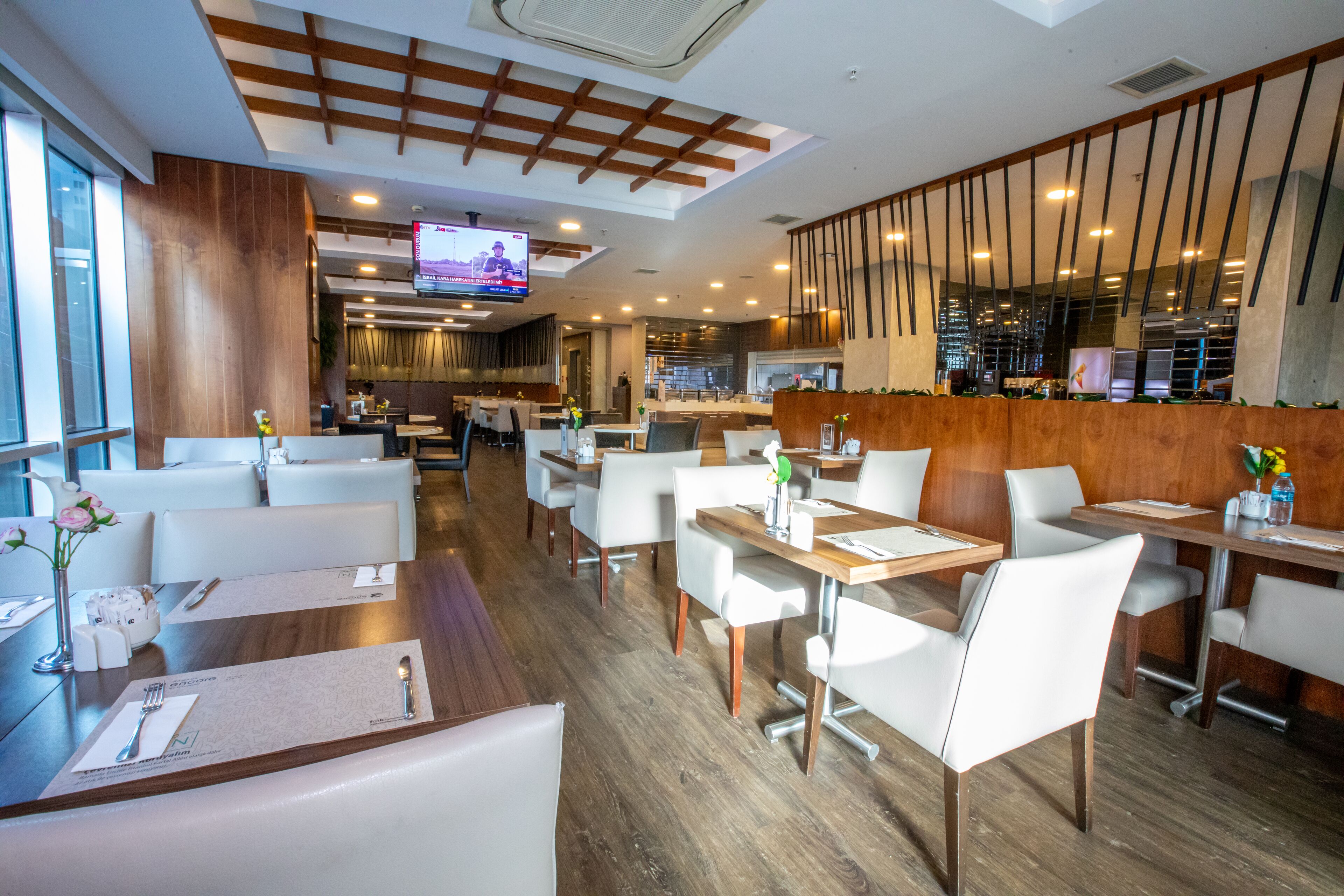 A modern restaurant with wooden flooring, white chairs, and tables set for dining.