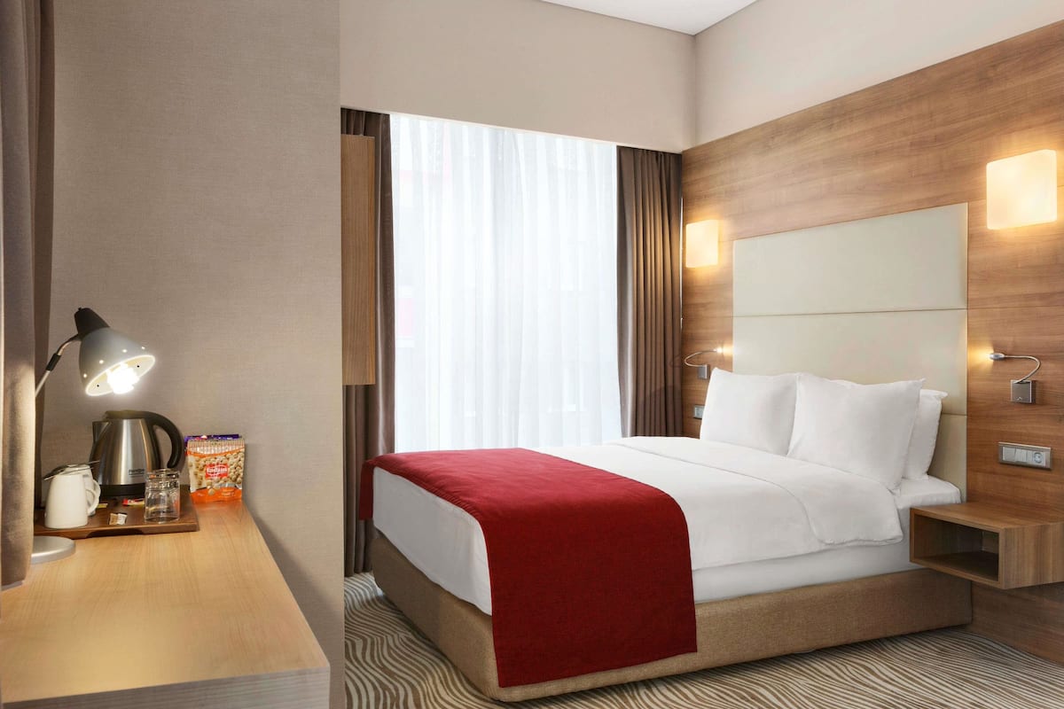 A hotel room with a bed, bedside table, lamp, and a large window with curtains.