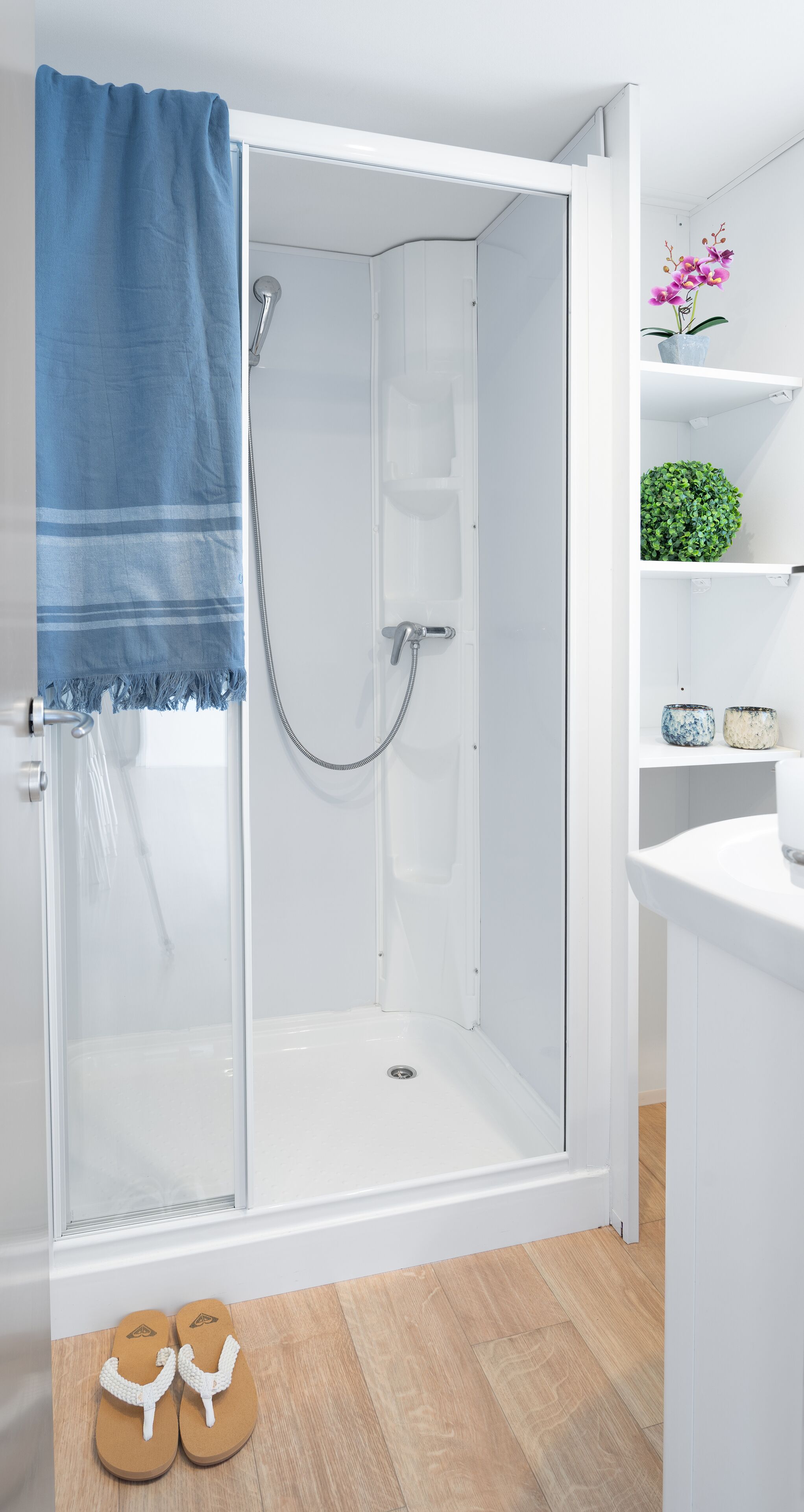 Un baño moderno con cabina de ducha de vidrio, sanitarios blancos y suelo de madera.