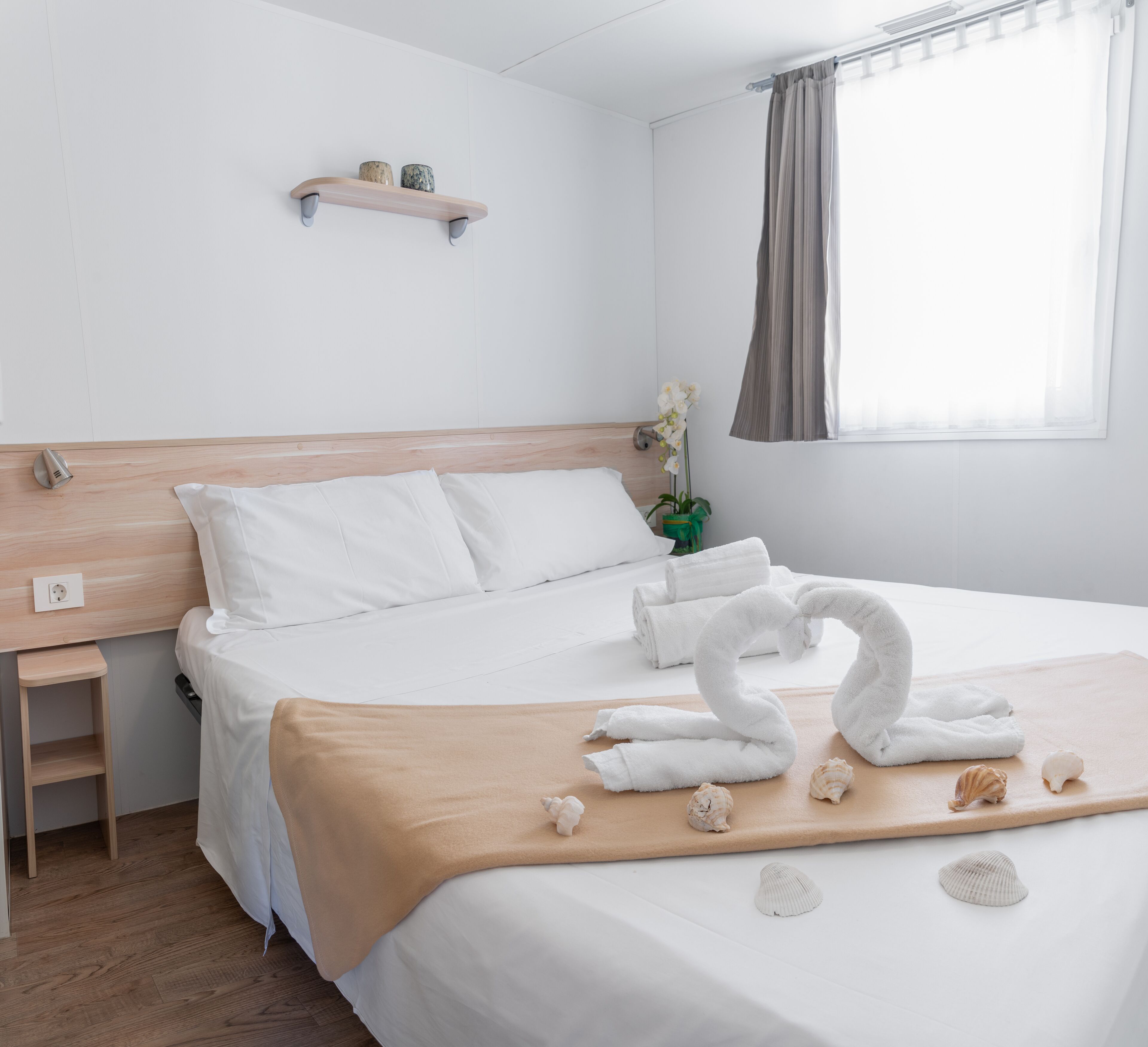 Una cama bien hecha con sábanas blancas, un cabecero de madera y una decoración de toallas con forma de cisne sobre una colcha color beige.