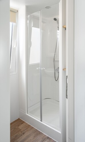 Eine Dusche mit Glastrennwand, einer Handbrause, einer weißen Tür und einem Holzboden.