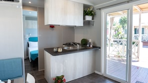 A modern kitchen with a central island, a dining area with a blue table, and a view of the outdoor deck. - Campingvillaggio Atlanta e Mediterraneo - Campground (Chioggia)