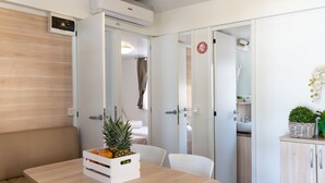 A modern, well-lit room with a wooden table, a white chair, and a bench. There is a small plant on the table and a basket on the bench. The room has white walls and a wooden ceiling. - Campingvillaggio Atlanta e Mediterraneo - Campground (Chioggia)