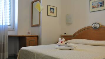 Quarto de hotel com cama, cabeceira de madeira, mesa de cabeceira, espelho e relógio fixado na parede.