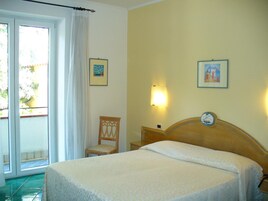 Una habitación de hotel con una cama, una silla, un reloj en la pared y dos cuadros enmarcados.