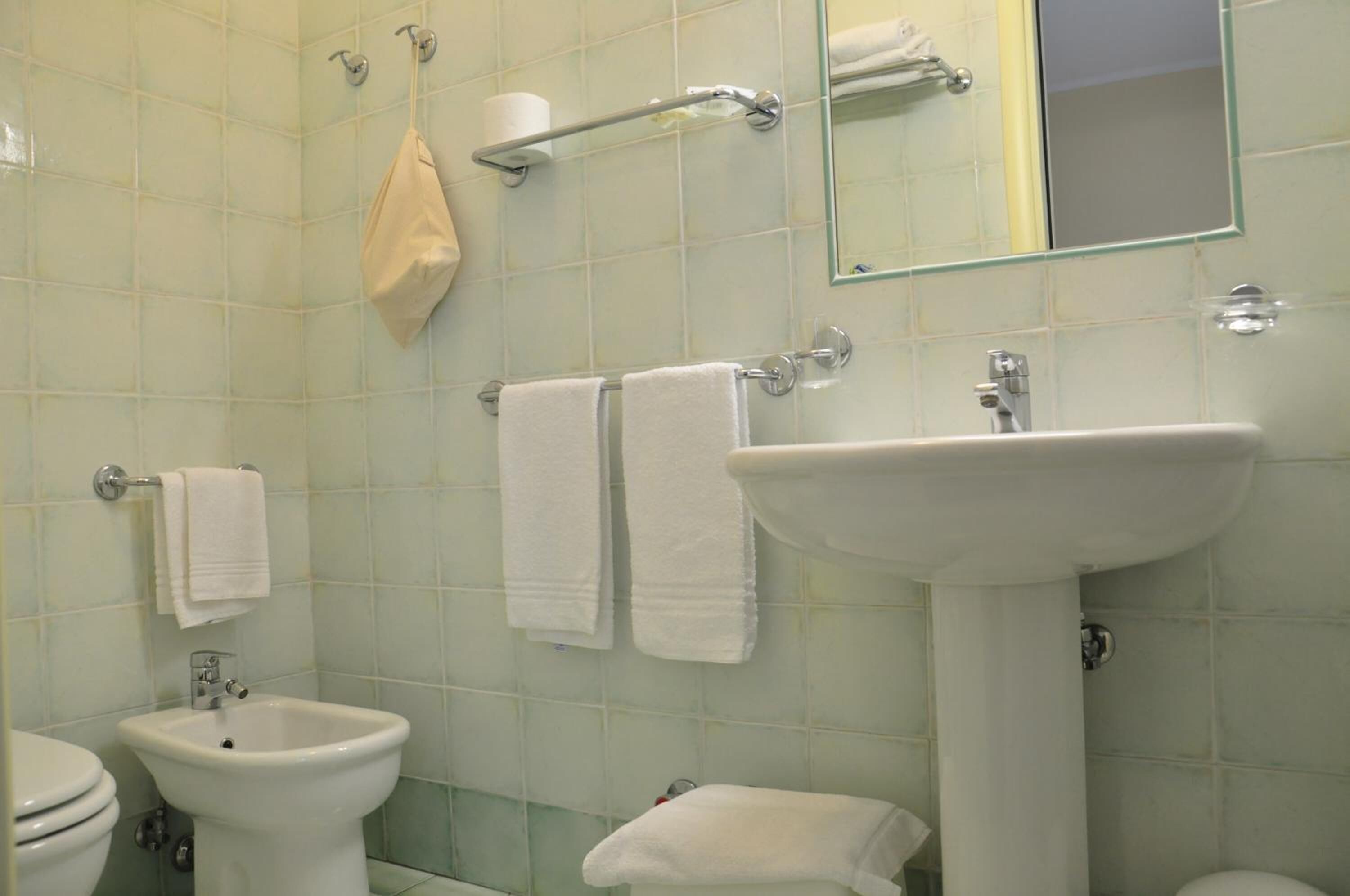 A bathroom with a bidet, a sink, and two towels hanging on towel bars.
