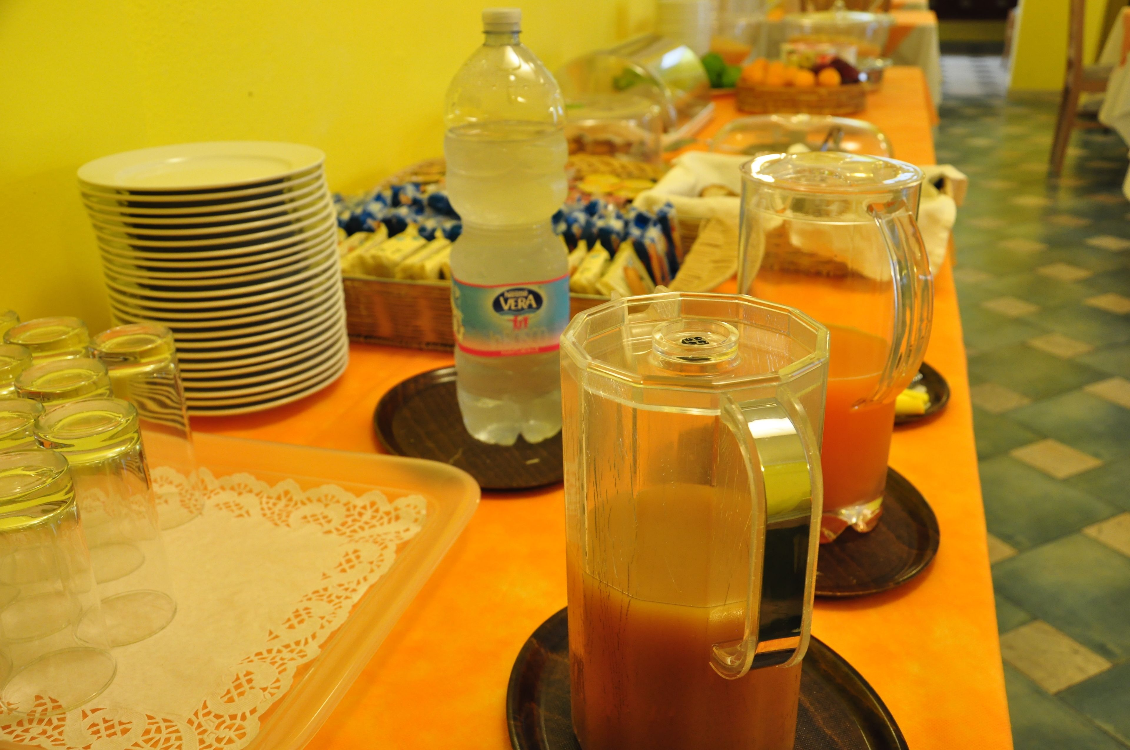 Un tavolo da buffet con piatti, una bottiglia d'acqua, una caraffa di succo e un vassoio con bicchieri.