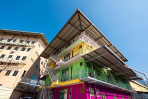 Un immeuble à plusieurs étages, doté d’une façade verte et jaune, de nombreux balcons et d’un espace d’accueil bien visible.