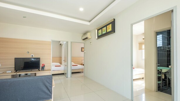 Una habitación de hotel moderna con televisión de pantalla plana, un escritorio con silla, dos camas, un baño con lavamanos y espejo, y un cuadro en la pared.