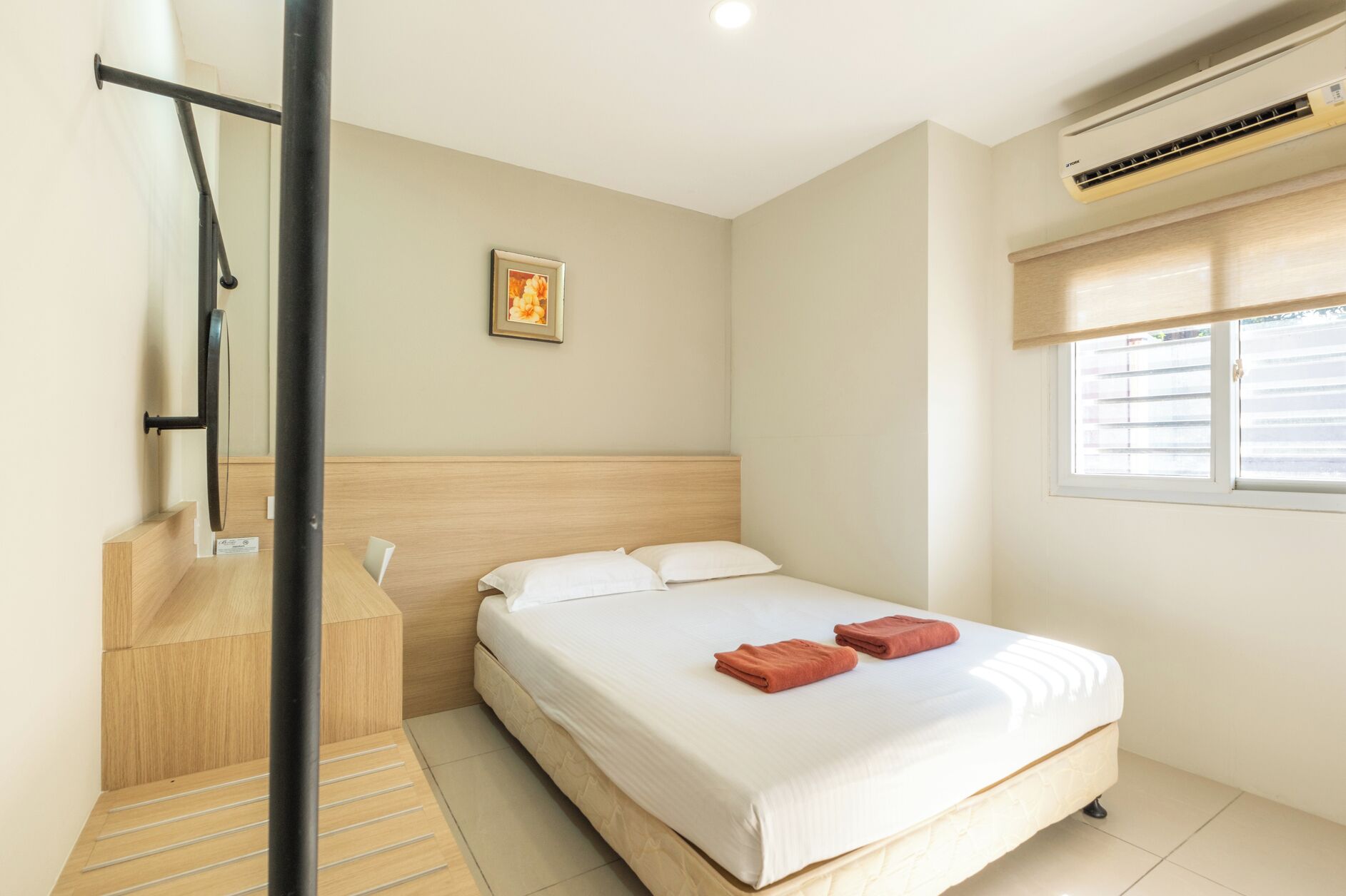 A hotel room with a bed, a window with blinds, an air conditioning unit, and a framed picture on the wall.