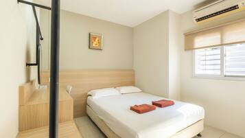 A hotel room with a bed, a window with blinds, an air conditioning unit, and a framed picture on the wall.