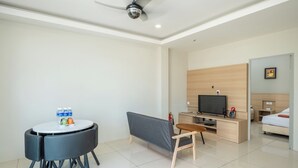 Una habitación de hotel moderna con una mesa de comedor redonda, un sofá gris, un televisor y una cama.