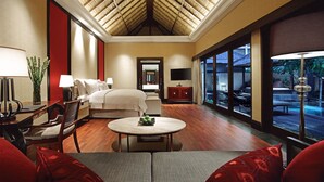 Habitación de hotel con cama, zona de estar con mesa, televisor y ventanas amplias con vistas al exterior.