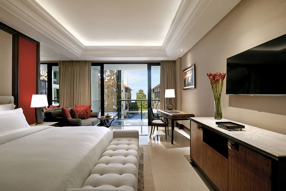 A hotel room with a large bed, a desk, a television, and a view of the outside.