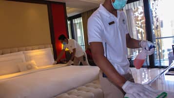 A hotel room with a large bed, a sofa, and a person cleaning the room.