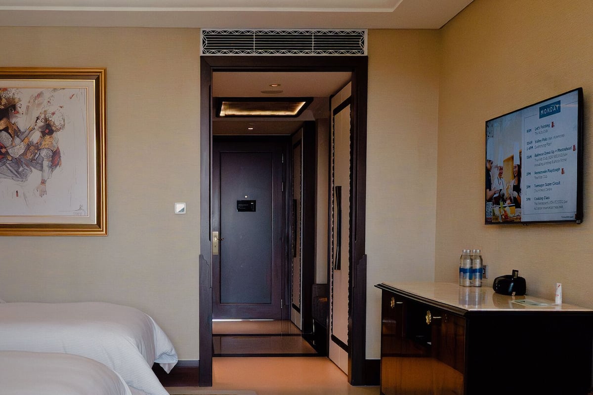 A hotel room with a bed, a desk, a chair, a framed picture, and a wall-mounted menu board.