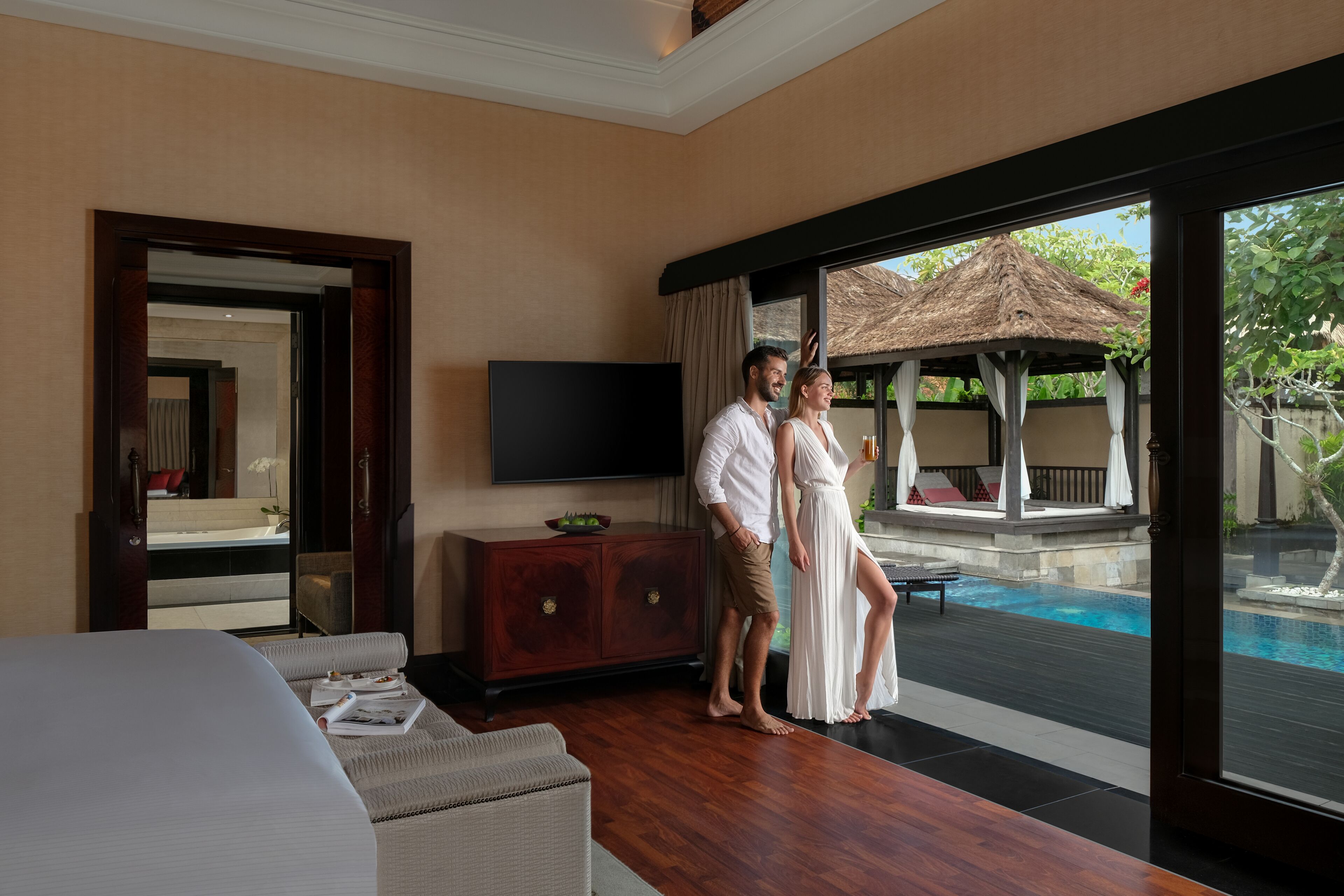 A hotel room with a large window, a TV, a wooden cabinet, and a pool view.