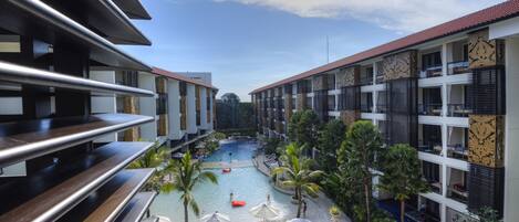 A modern hotel with a central swimming pool, outdoor seating, and lush greenery.