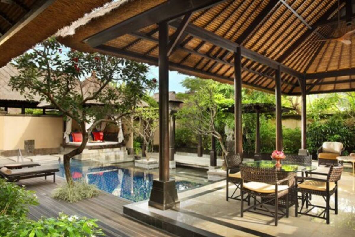A pool area with a thatched roof, lounge chairs, and wicker furniture.