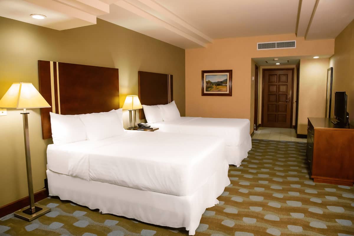 A hotel room with two beds, a desk, a TV, and a painting on the wall.
