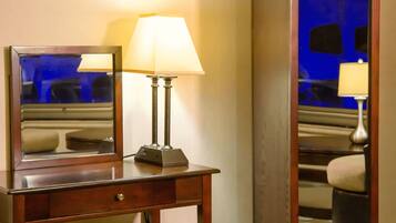 A hotel room with a desk, chair, lamp, and a mirror.