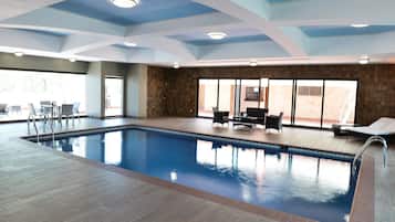 Una piscina interior con suelo de baldosas, rodeada de sillas y una tumbona.