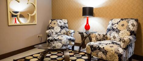 A room with two floral armchairs, a small round table, a red lamp, and a patterned rug.