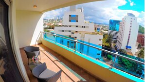 Un balcón con sillas de mimbre y una pequeña mesa, con vistas a un paisaje urbano con edificios modernos.
