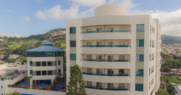 Un hotel de varios pisos con balcones, una terraza en la azotea y vistas a un pueblo en la ladera.