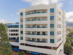 Un hotel de varios pisos con balcones, mobiliario exterior y vistas a la ciudad.