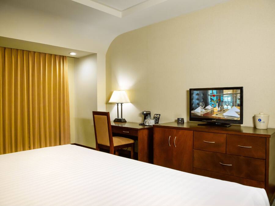 A hotel room with a bed, a desk with a lamp, a television, and a cabinet.
