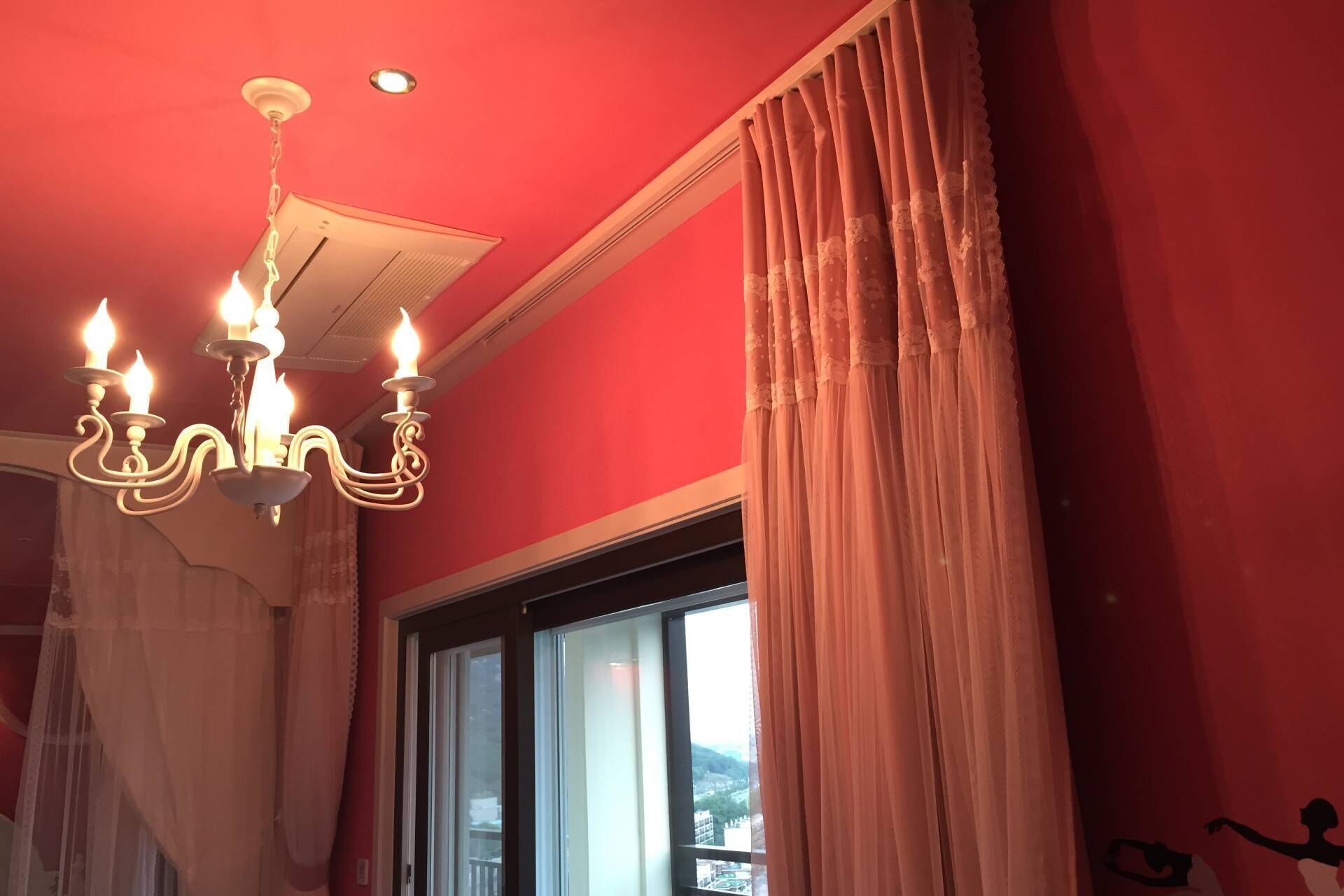 A room with a chandelier, a window with curtains, and a red wall.