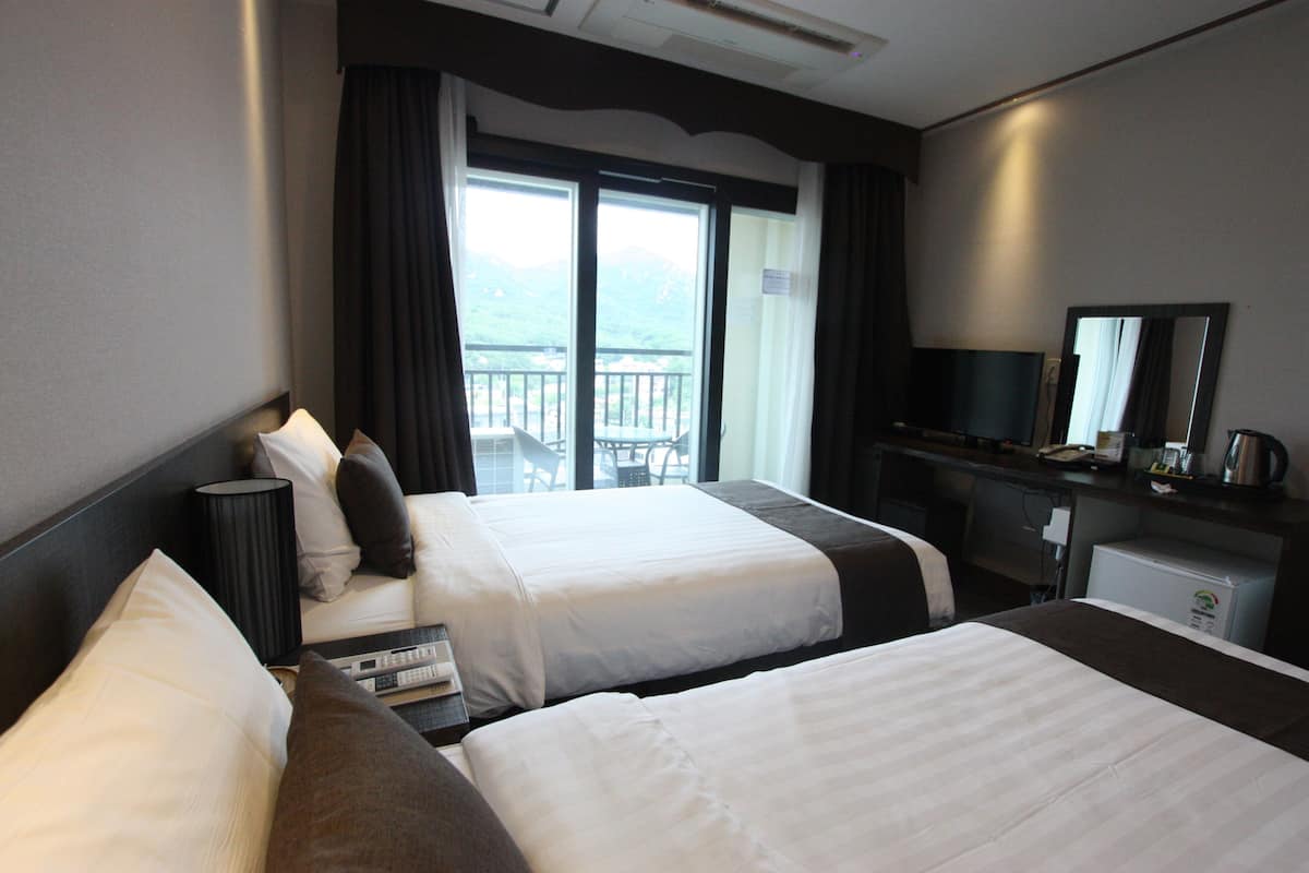 Ein Hotelzimmer mit zwei Betten, einem Schreibtisch, einem Fernseher und einem Balkon mit Blick.